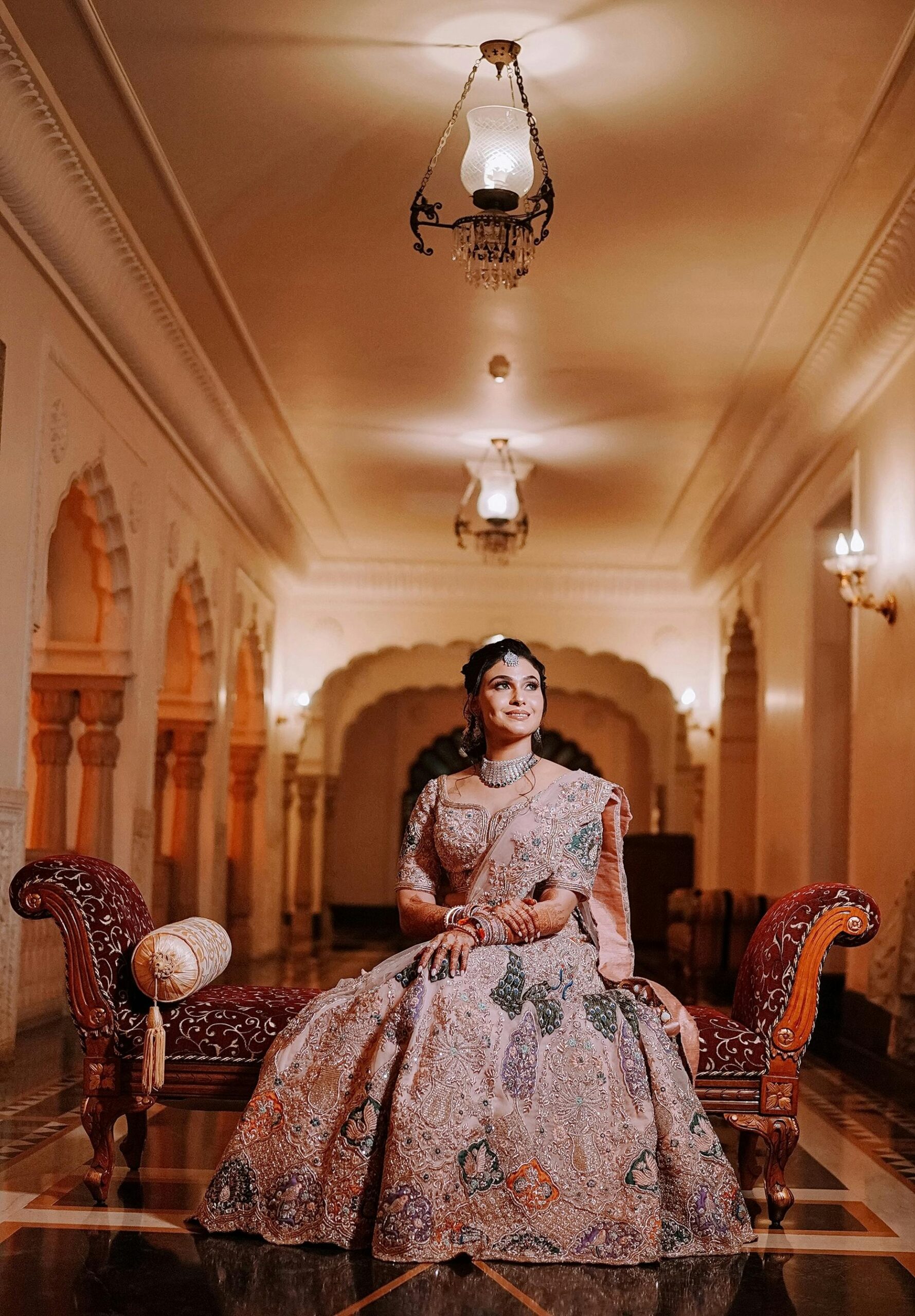 A stunning Indian bride in traditional attire poses gracefully in a beautiful Jaipur palace.