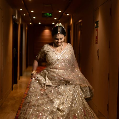 A stunning bride walking gracefully in a sparkling traditional Indian lehenga indoors.